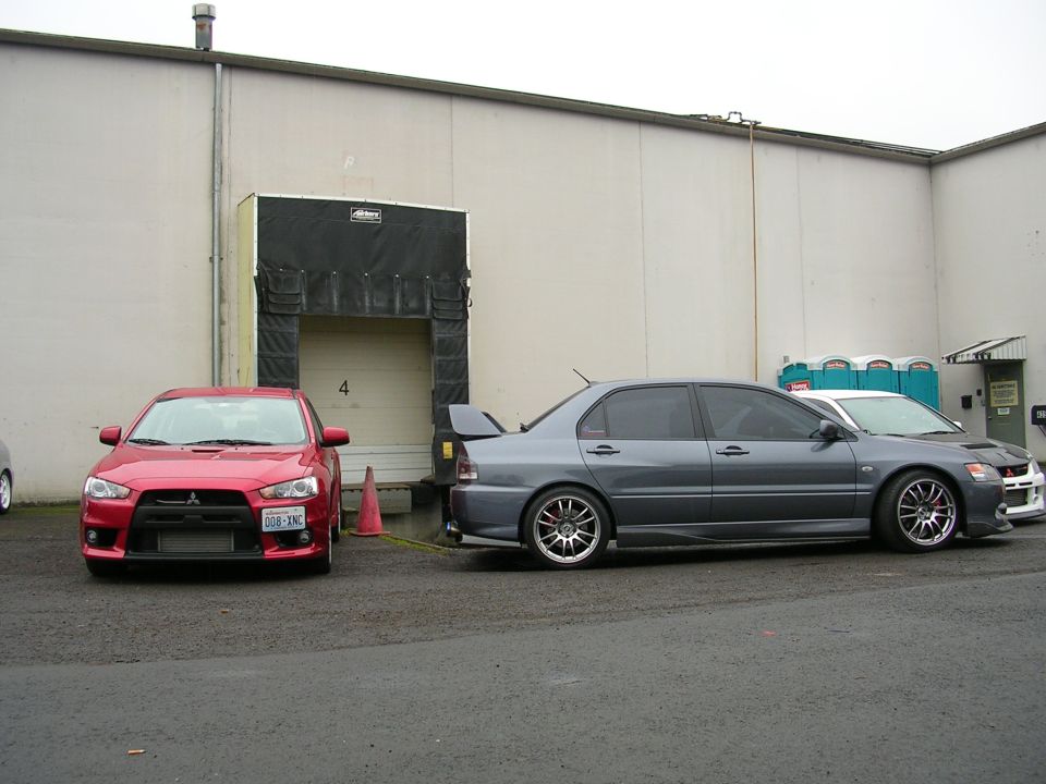 Red and gray Mitsubishi Lancer Evolutions parked outside a warehouse.
