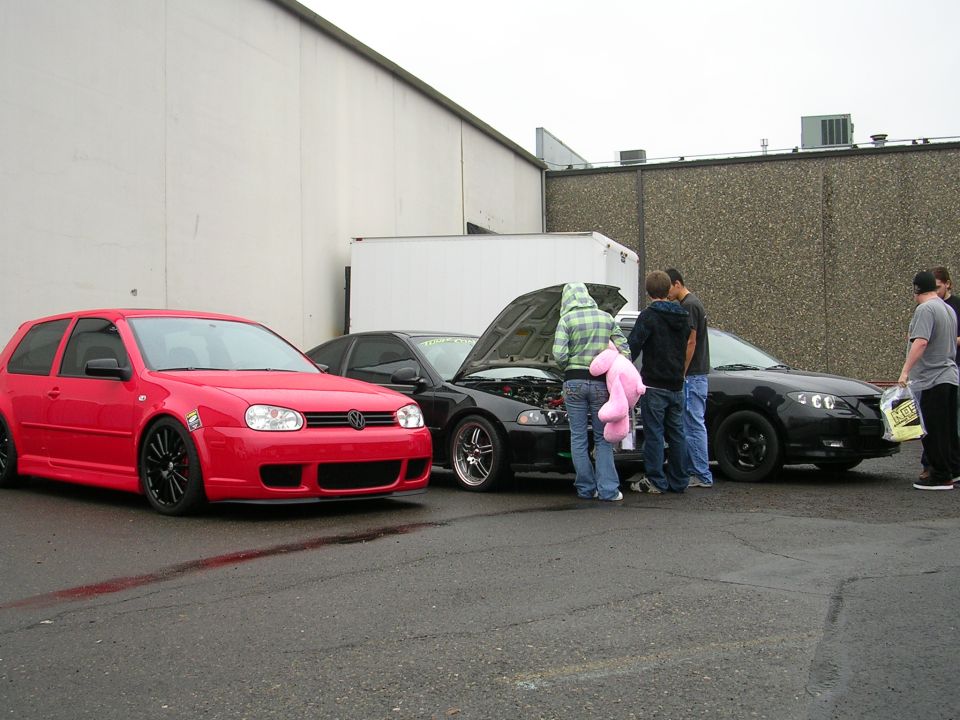 Red Volkswagen Golf GTI and black Mazda 3 with hood open, people gathered around.