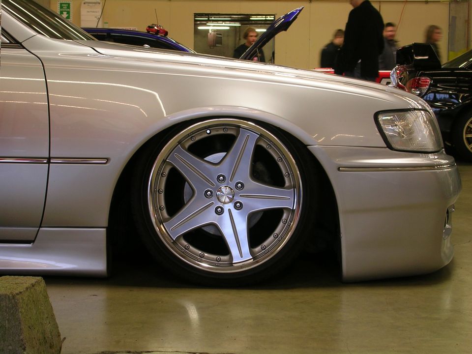 Silver sedan with custom chrome wheel, lowered suspension, front passenger side view.