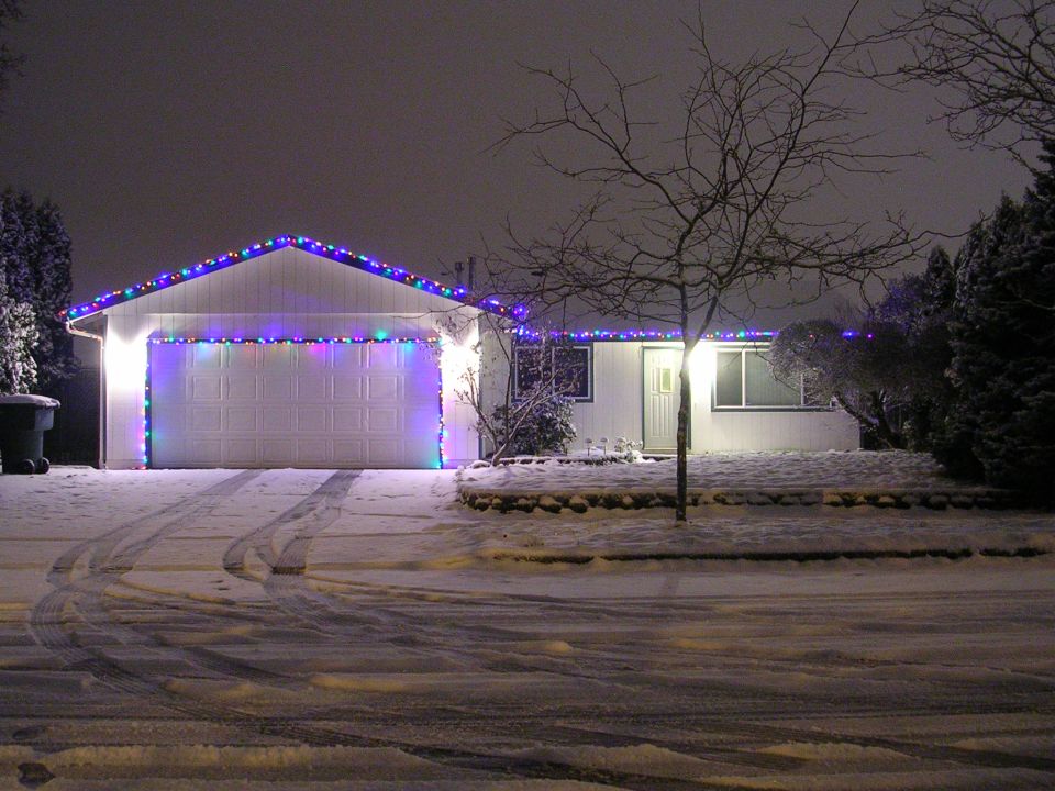A house decorated with Christmas lights in the snow at night.