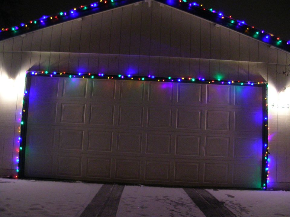 Garage door decorated with colorful Christmas lights in the snow.