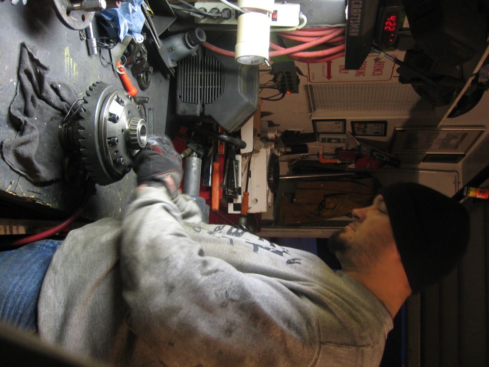 Man holding a differential ring gear assembly inside a garage