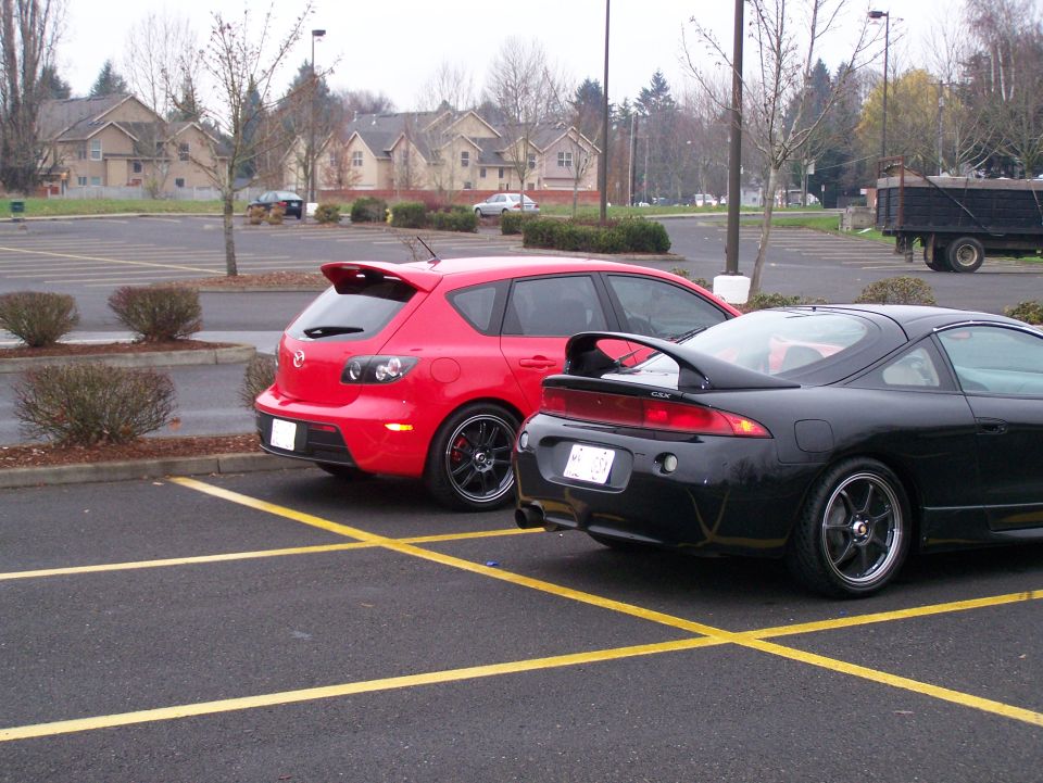 Red Mazda 3 hatchback and black Mitsubishi Eclipse coupe parked in a lot.