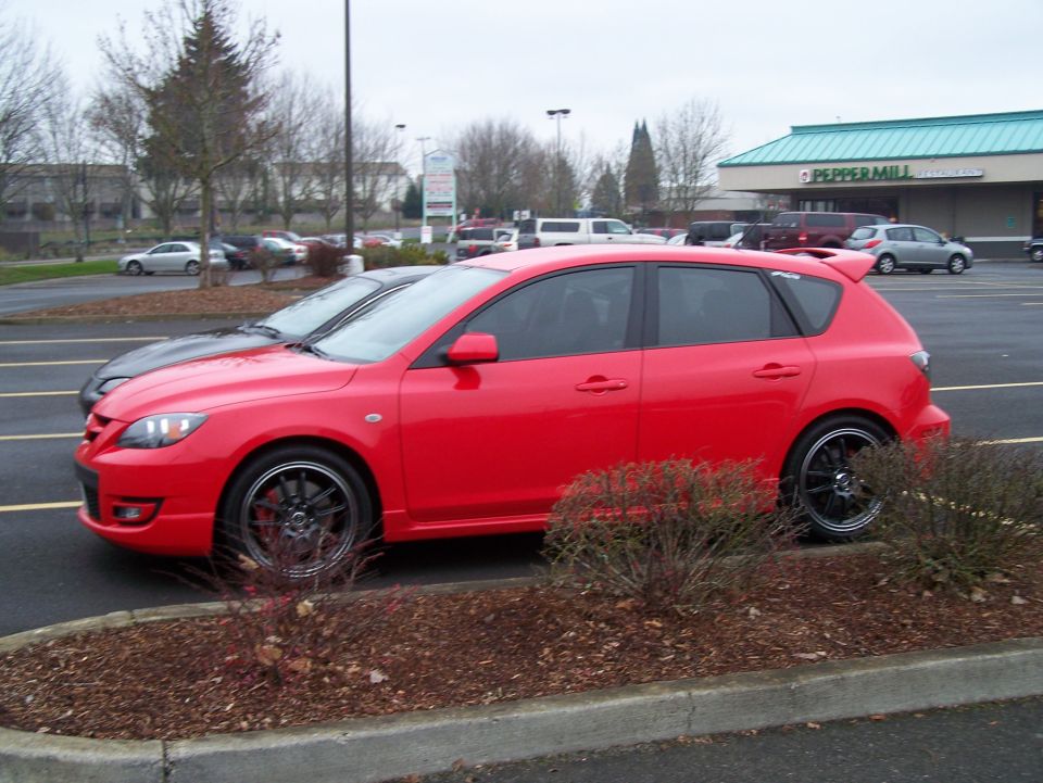 Red Mazda 3 hatchback parked in a lot.