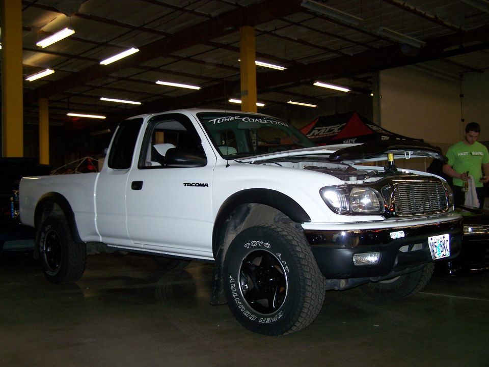 White Toyota Tacoma pickup truck with hood open, parked indoors.