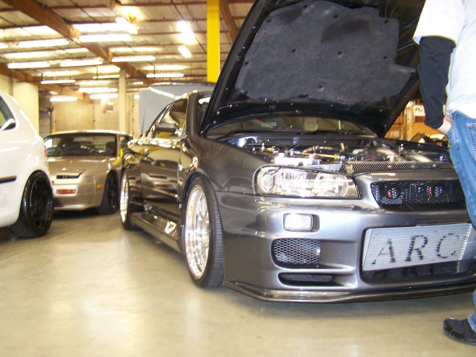 Dark gray Nissan Skyline GT-R R34 with hood open, parked indoors.
