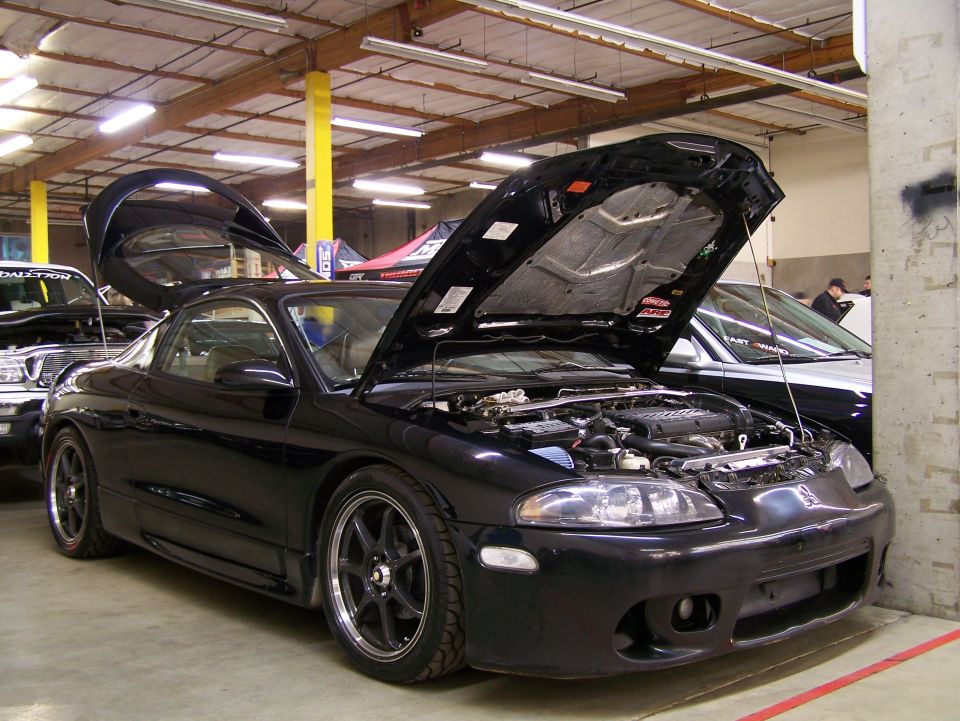 Black Mitsubishi Eclipse coupe with hood and door open, engine visible.