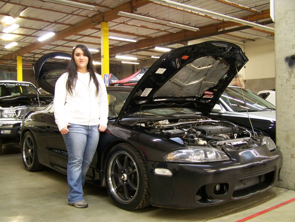 Woman standing next to a black Mitsubishi Eclipse with the hood open.