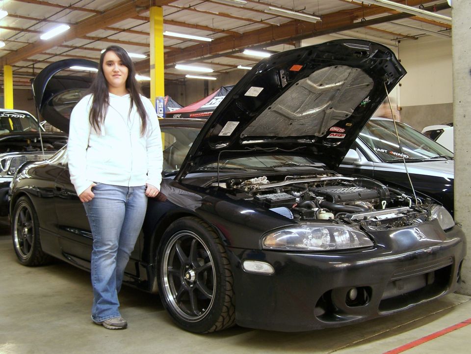 Black Mitsubishi Eclipse coupe with hood open at indoor car show, person standing beside it