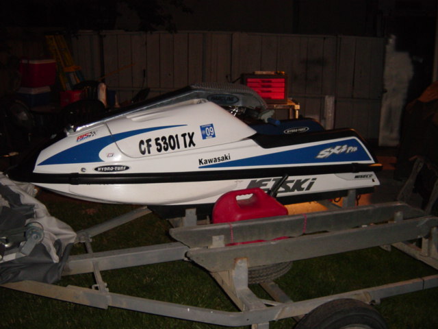 White and blue Kawasaki SXi Pro stand-up jet ski on trailer at night, side view