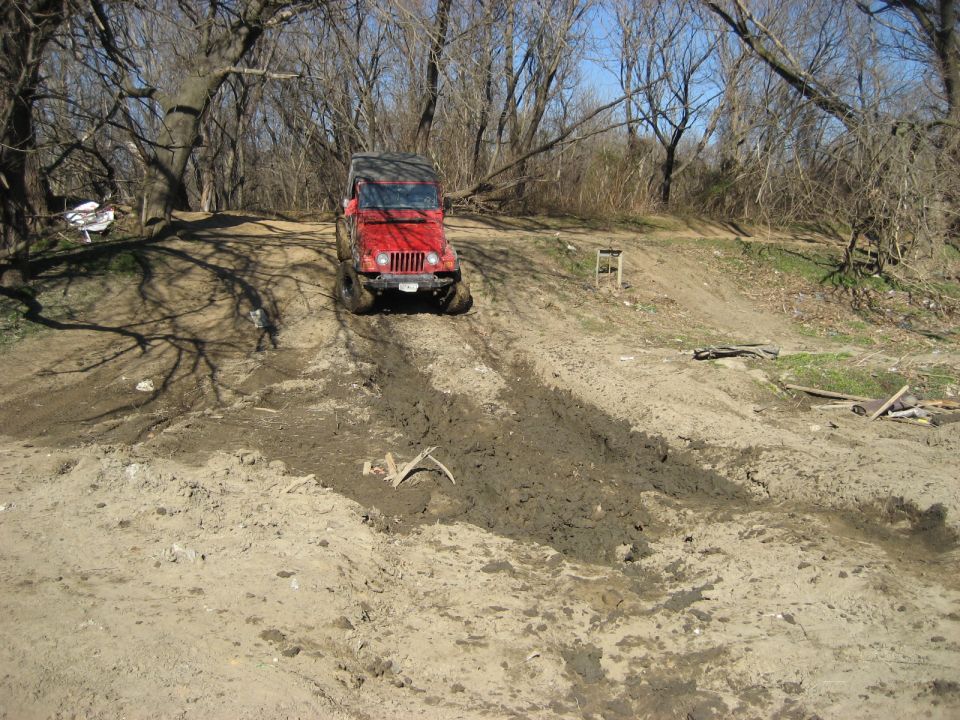 Red Jeep Wrangler driving up a muddy hill.
