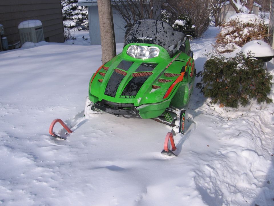 Green Arctic Cat snowmobile with red skis parked in snow, front three-quarter view