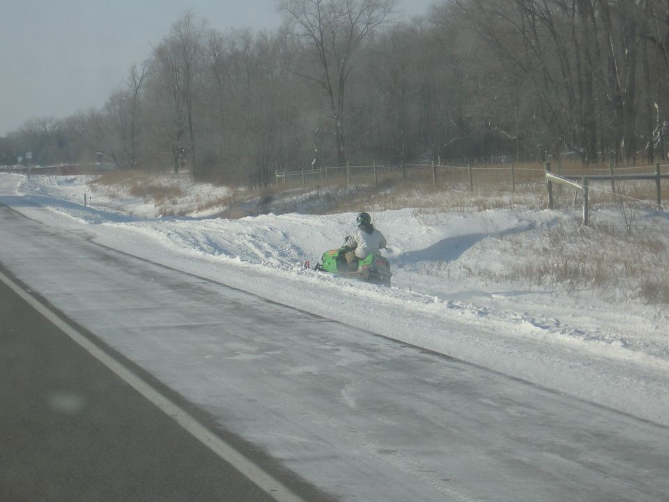 Rider on a green snowmobile in the snowy ditch alongside a plowed highway