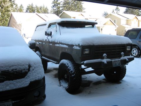 1979 Ford Bronco - A brown Ford Bronco covered in snow sits parked next to another snow-covered vehicle. The Bronco has large tires and a custom bumper with a…