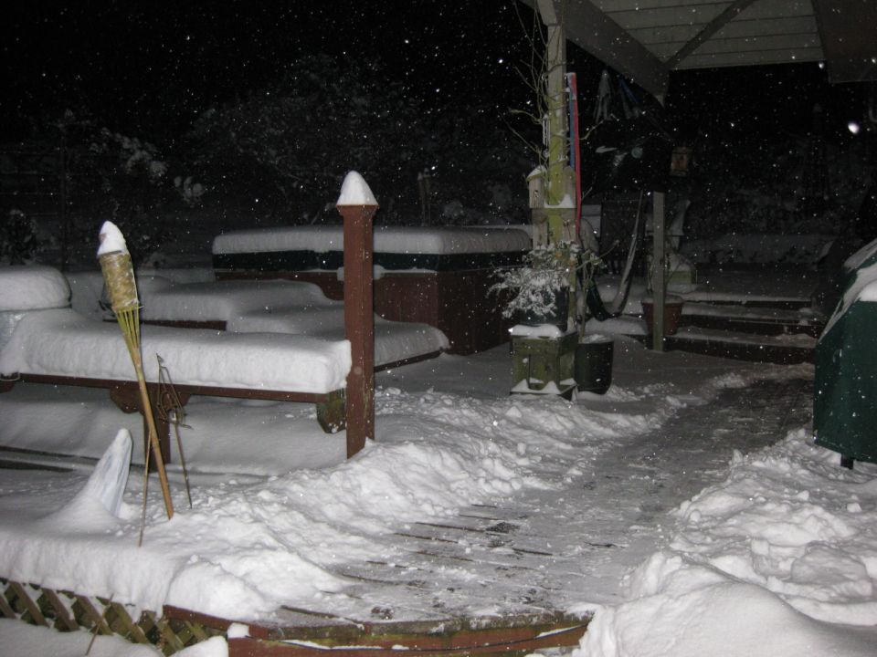Snow covered backyard at night with a hot tub and patio furniture.