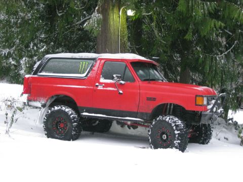 1979 Ford Bronco - A red Ford Bronco is parked in the snow with large off-road tires and a Monster Energy sticker on the rear window. The vehicle is surrounde…