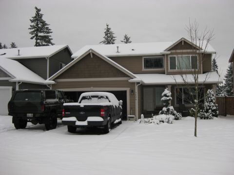 1979 Ford Bronco - A dark green Ford Bronco and a black Ford F-150 pickup truck are parked in a snowy driveway in front of a house. The vehicles are covered i…