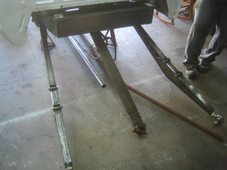 Vehicle body on a rotisserie stand with suspension links and a driveshaft on a garage floor