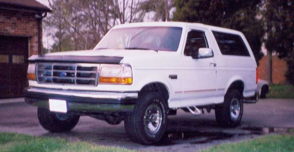 White Ford Bronco with a black bug deflector and chrome wheels parked on a driveway