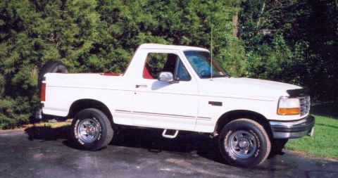 1993 Ford Bronco - A white 1993 Ford Bronco is shown from a 3/4 front angle, parked outdoors with trees in the background.