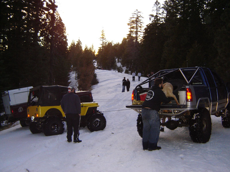 Group of off-road vehicles and people in a snowy forest clearing at sunset