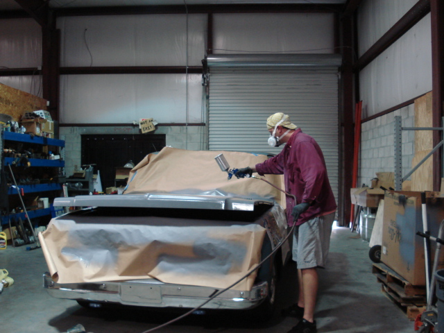 Person spray painting a classic pickup truck in a workshop.