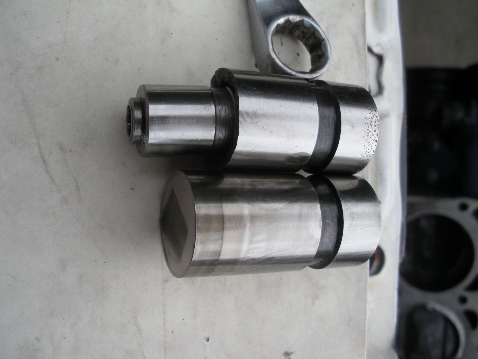 Two metal engine parts, possibly camshaft lifters, with a wrench.