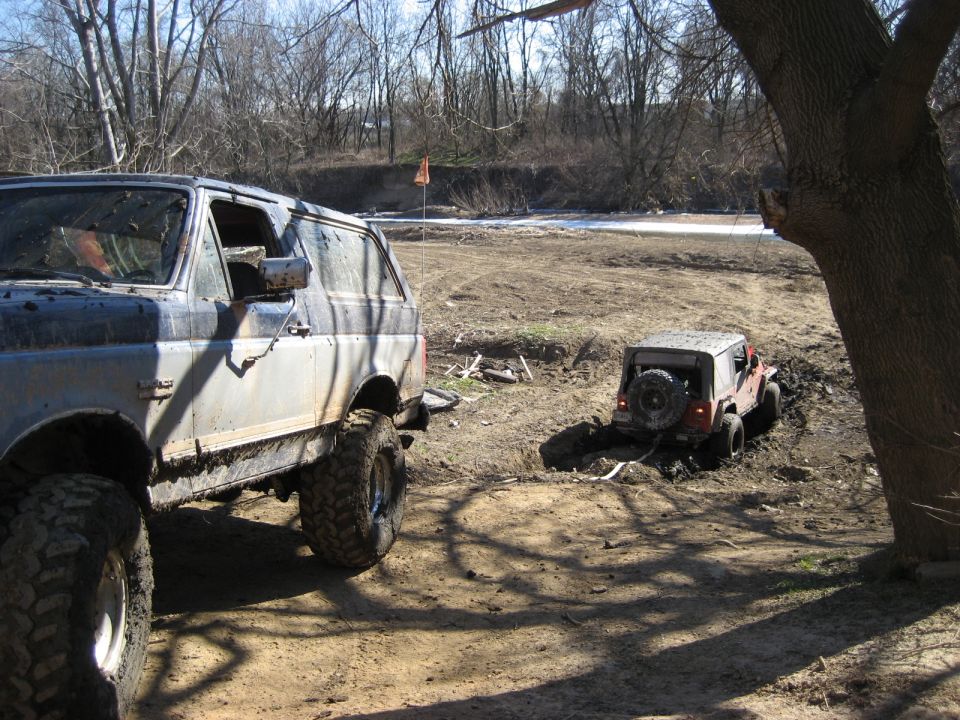 Muddy 1991 Ford Bronco and a red Jeep stuck in the mud.