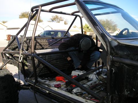 1986 Toyota Hilux - A person is working inside the modified interior of a vehicle, which features a prominent roll cage and large off-road tires visible. The v…