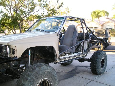 1986 Toyota Hilux - A custom-built off-road vehicle, likely a Toyota Hilux, is shown from the front three-quarter view. The vehicle features a stripped-down bo…