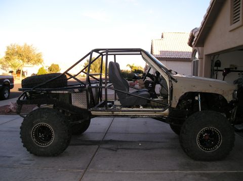 1986 Toyota Hilux - Side view of a heavily modified off-road vehicle, likely a Toyota Hilux, with a custom roll cage, large tires, and an exposed interior. The…