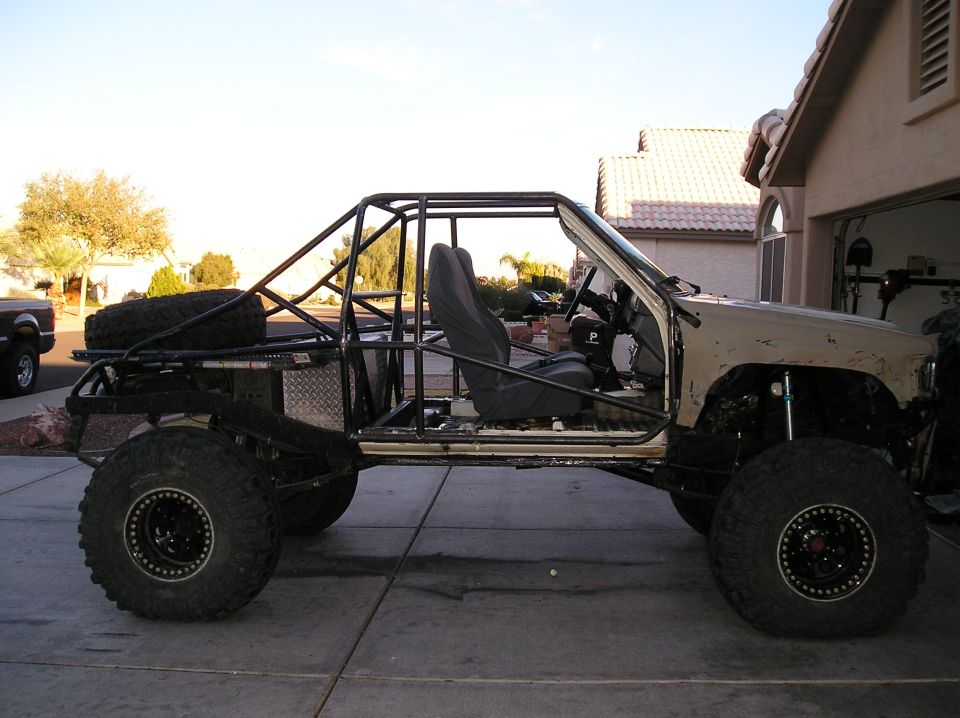 Modified Toyota Hilux with roll cage and large tires, parked on driveway.