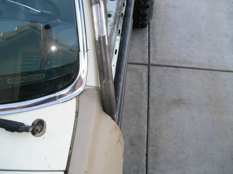 1986 Toyota Hilux - Close-up view of the driver's side A-pillar and windshield trim of a white vehicle, with a metal roll cage tube visible. The vehicle is par…