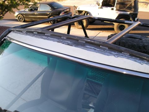 1986 Toyota Hilux - A custom roll cage is welded onto the roofline of a white vehicle, partially obscuring the interior. In the background, a black sedan and a…