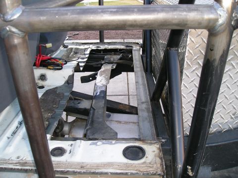 1986 Toyota Hilux - The interior of a vehicle is shown, with the floor removed to expose the chassis and roll cage components. Wires and metal framing are visi…