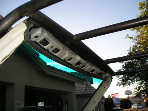 1986 Toyota Hilux - A custom roll cage made of dark metal tubing is installed over the open top of a white vehicle. The interior structure above the windshield…