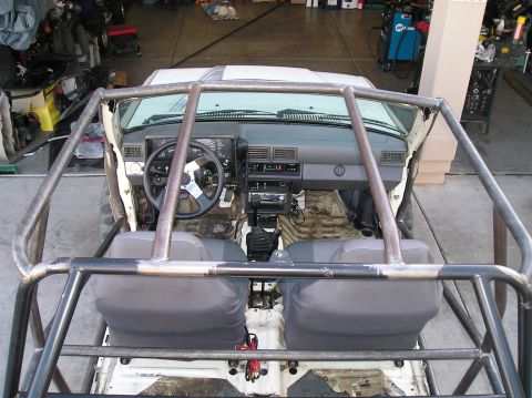 1986 Toyota Hilux - The interior of a modified Toyota Hilux pickup truck is shown from an overhead perspective, featuring a roll cage, aftermarket steering whe…
