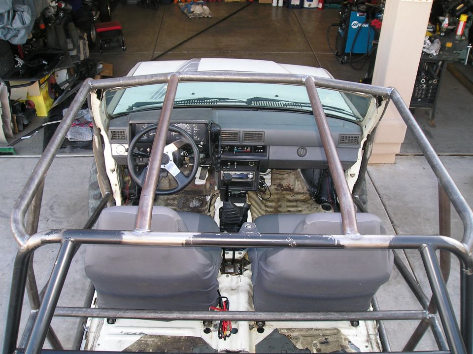 Overhead view of a modified Toyota Hilux interior with roll cage, aftermarket steering wheel, and exposed floor.