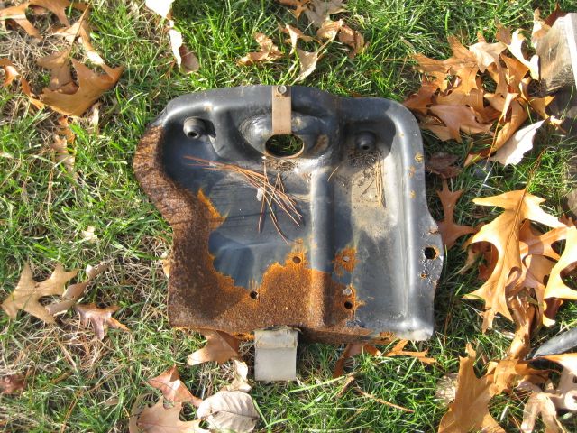 Rusty black metal car part on grass with fallen leaves