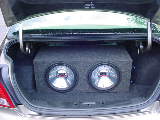 Two MTX subwoofers in a carpeted box installed in the open trunk of a gold sedan