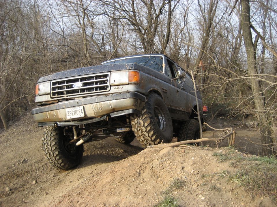 Lifted dark 1991 Ford Bronco driving off-road on a dirt path.