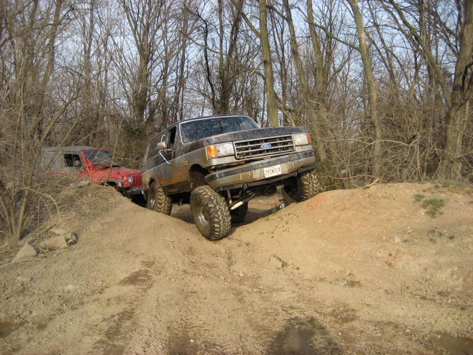 Muddy 1991 Ford Bronco climbing a dirt hill in a forest.