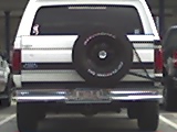 1996 Ford Bronco - The rear view of a white Ford Bronco is shown, featuring a spare tire mounted on the tailgate and a chrome bumper. The vehicle is parked in…