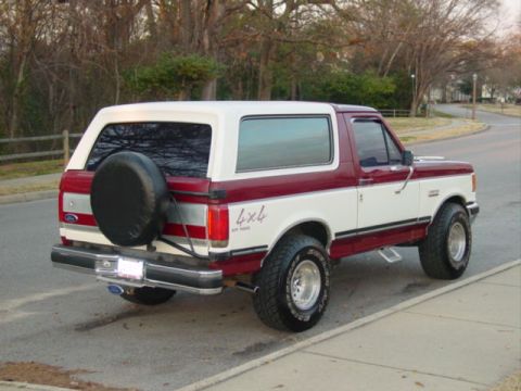 1988 Ford Bronco - This two-tone Ford Bronco is parked on a residential street with trees in the background.