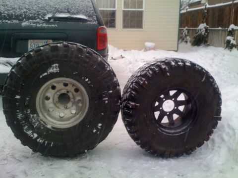1983 Ford Bronco - Two large off-road tires are displayed in the snow, with a dark green minivan visible in the background.
