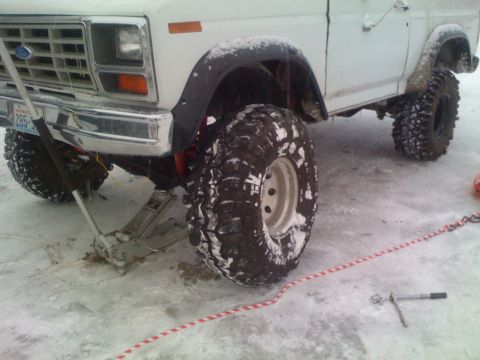1983 Ford Bronco - A white 1983 Ford Bronco is shown with large off-road tires, jacked up in a snowy environment.