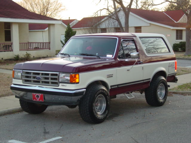Maroon and white Ford Bronco parked on asphalt, front 3/4 view. Visible "4x4" decal on rear quarter panel