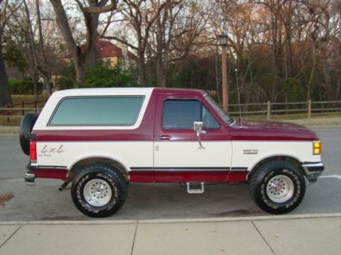 1988 Ford Bronco - This two-tone red and white Ford Bronco features a side view and prominent 4x4 badging, consistent with the 1988 model year.