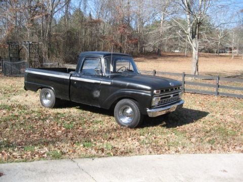 1966 Ford F-100 - This black 1966 Ford F-100 pickup truck is parked outdoors on a sunny day.