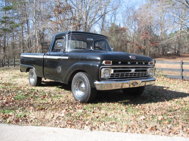 Black 1966 Ford F-100 pickup truck parked on grassy area with trees in background